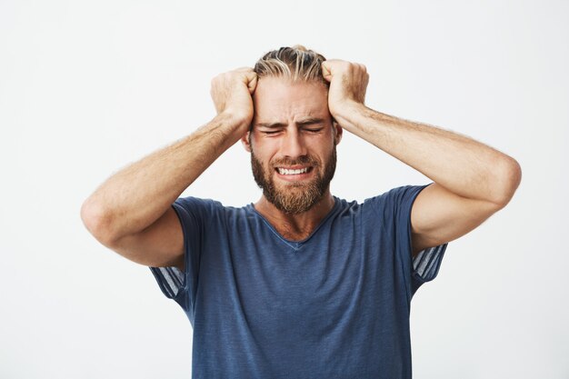 Portrait de beau mec nordique avec coupe de cheveux à la mode et barbe tenant la tête avec les mains souffrant de maux de tête