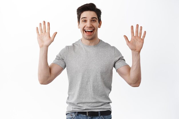 Portrait d'un beau mec sympathique dit bonjour, agitant les mains et souriant, saluant ou faisant un geste d'adieu, debout optimiste sur fond blanc