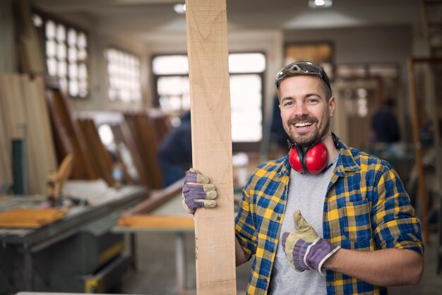 Portrait de beau menuisier souriant avec des matériaux en bois à l'atelier holding Thumbs up