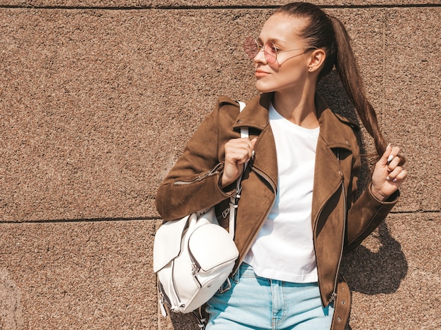 Portrait de beau modèle brune souriante habillée en veste d'été hipster et vêtements jeans