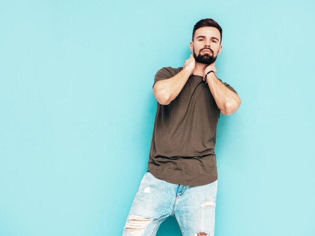 Portrait de beau modèle confiant hipster élégant hipster lambersexual Homme vêtu d'un t-shirt et d'un jean Mode homme isolé sur mur bleu en studio