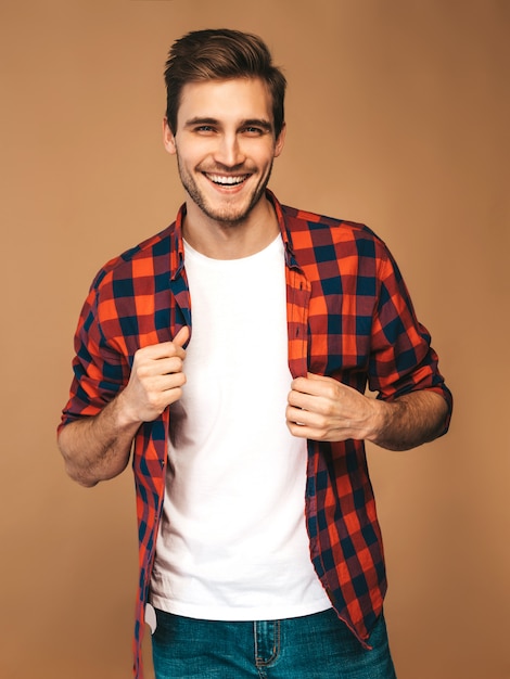 Portrait de beau modèle élégant jeune homme souriant vêtu d'une chemise à carreaux rouge. Homme de mode posant