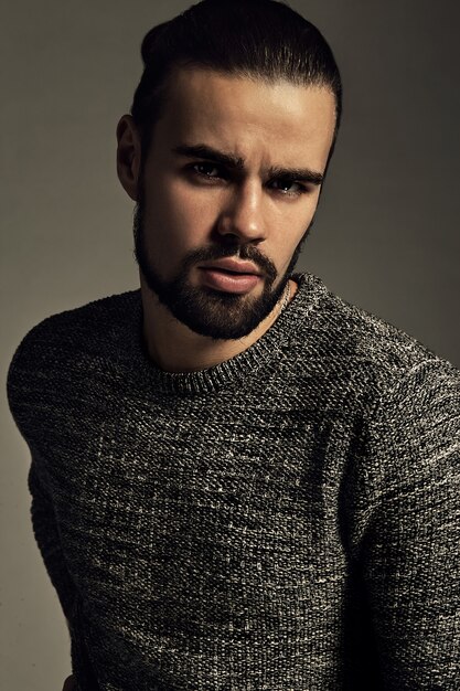 portrait de beau modèle hipster élégant de mode vêtu d'un pull chaud qui pose en studio.