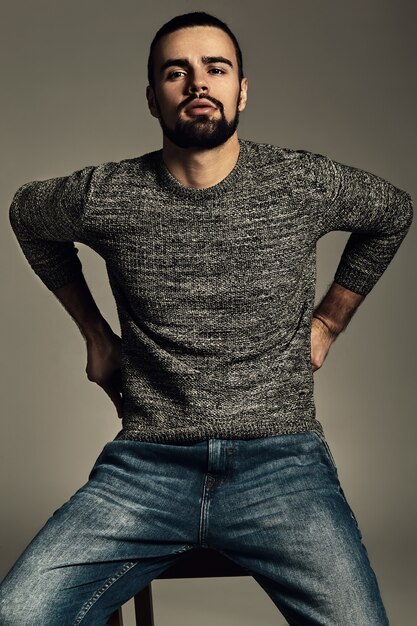 portrait de beau modèle hipster élégant de mode vêtu d'un pull chaud qui pose en studio.