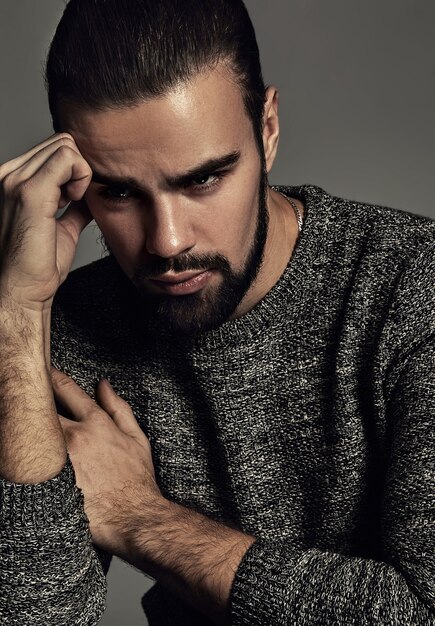 portrait de beau modèle hipster élégant de mode vêtu d'un pull chaud qui pose en studio.