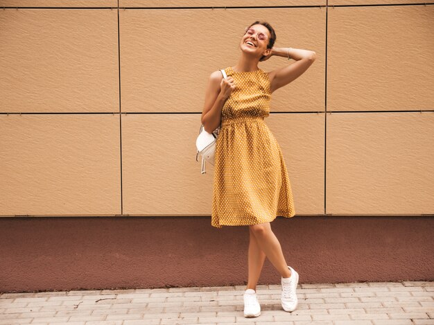 Portrait de beau modèle hipster souriant vêtu d'une robe d'été jaune. Fille branchée posant dans la rue. Femme drôle et positive s'amuser
