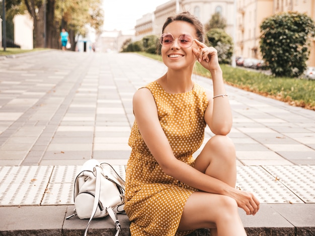 Portrait de beau modèle hipster souriant vêtu d'une robe d'été jaune. Fille branchée posant dans la rue. Femme drôle et positive s'amuser