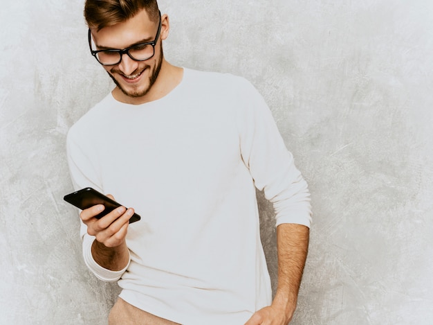 Portrait de beau modèle d'homme d'affaires souriant hipster portant des vêtements décontractés d'été blanc .. avec téléphone portable