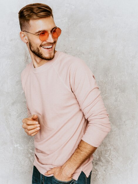 Portrait de beau modèle jeune homme souriant portant des vêtements décontractés d'été rose. Homme élégant de mode posant dans des lunettes de soleil rondes