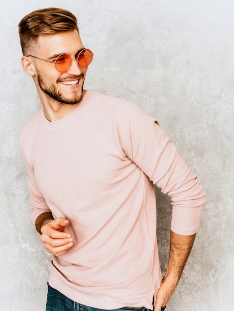 Portrait de beau modèle jeune homme souriant portant des vêtements décontractés d'été rose. Homme élégant de mode posant dans des lunettes de soleil rondes