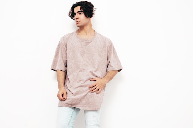 Portrait de beau modèle lambersexuel hipster élégant et confiant Homme sexy vêtu d'un t-shirt et d'un jean surdimensionnés Homme de mode isolé en studio Posant près d'un mur blanc