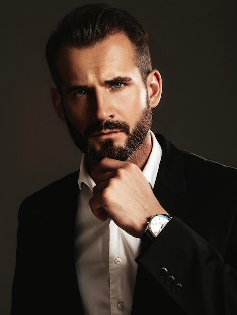 Portrait de beau modèle lambersexuel hipster élégant et confiant Sexy homme moderne vêtu d'un élégant costume noir Mode homme posant en studio sur fond sombre