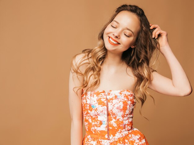 Portrait de beau modèle mignon souriant avec des lèvres roses. Fille en robe colorée d'été. Modèle posant. Jouer avec ses cheveux