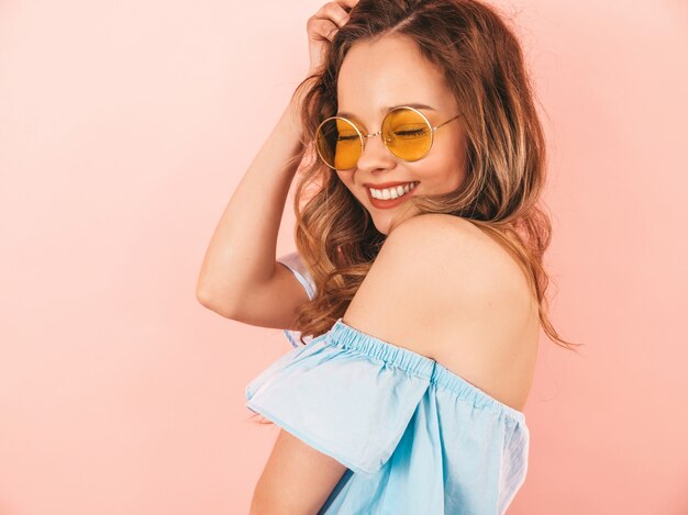 Portrait de beau modèle mignon souriant en lunettes de soleil rondes. Fille en vêtements colorés d'été. Modèle posant