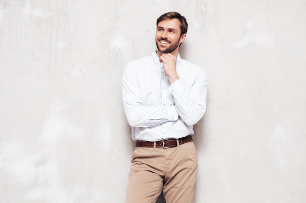 Portrait de beau modèle souriant Sexy homme élégant vêtu d'une chemise et d'un pantalon Mode hipster mâle posant près d'un mur gris en studio Isolé