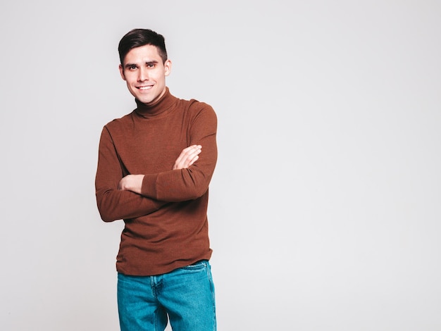 Portrait de beau modèle souriant Sexy homme élégant vêtu d'un pull à col roulé marron et d'un jean Mode hipster mâle posant en studio