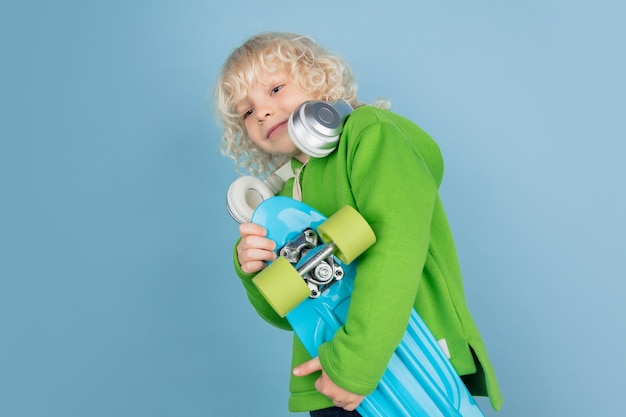 Portrait de beau petit garçon caucasien isolé sur fond bleu studio. Modèle masculin bouclé blonde. Concept d'expression faciale, émotions humaines, enfance, publicité, ventes.