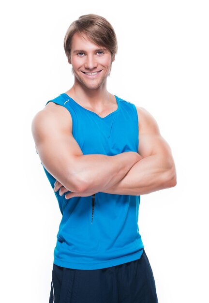 Portrait de beau sportif heureux en chemise bleue posant sur un mur blanc.