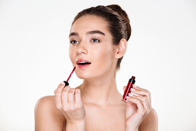 Portrait de beauté de l'élégante dame à moitié nue avec des cheveux en chignon appliquant du rouge à lèvres rouge