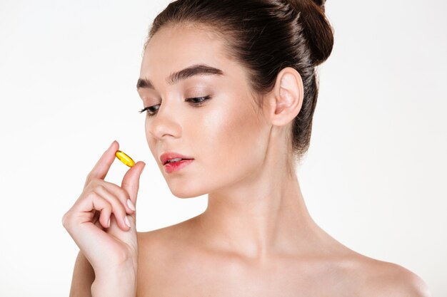 Portrait de beauté d'une femme assez concentrée avec une peau douce tenant une pilule dans sa main posant