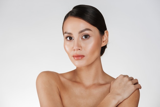 Portrait de beauté d'une femme à moitié nue regardant la caméra et touchant sa douce épaule, isolé sur blanc