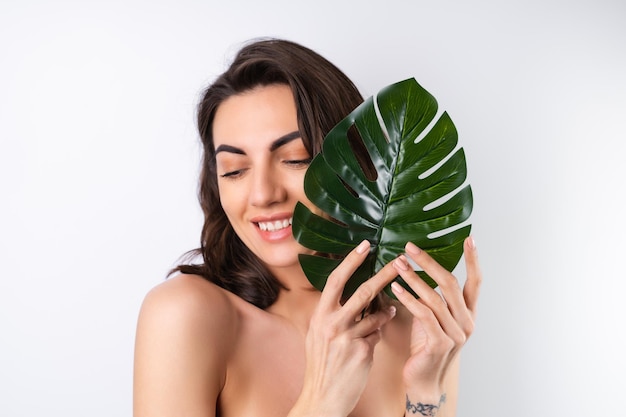 Portrait de beauté en gros plan d'une femme aux seins nus avec une peau parfaite et un maquillage naturel avec une feuille de palmier monstera