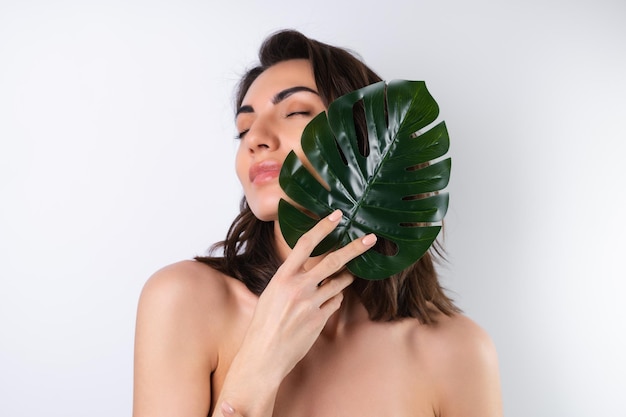 Portrait de beauté en gros plan d'une femme aux seins nus avec une peau parfaite et un maquillage naturel avec une feuille de palmier monstera