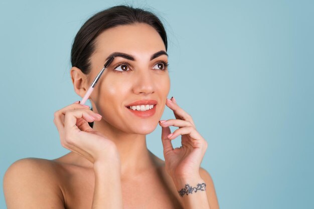 Portrait de beauté en gros plan d'une femme avec une peau parfaite et un maquillage naturel, des lèvres nues pleines, tenant une brosse à sourcils