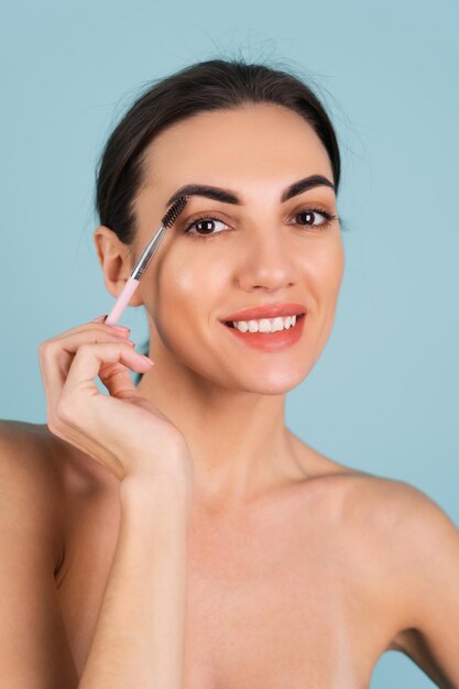 Portrait de beauté en gros plan d'une femme avec une peau parfaite et un maquillage naturel, des lèvres nues pleines, tenant une brosse à sourcils