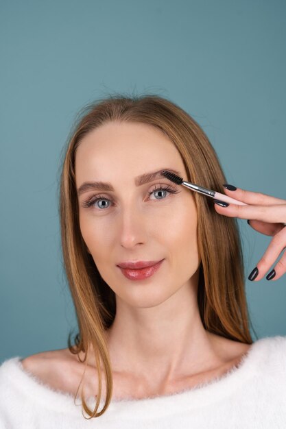 Portrait de beauté en gros plan d'une femme avec une peau parfaite et un maquillage naturel, des lèvres nues pleines, tenant une brosse à sourcils