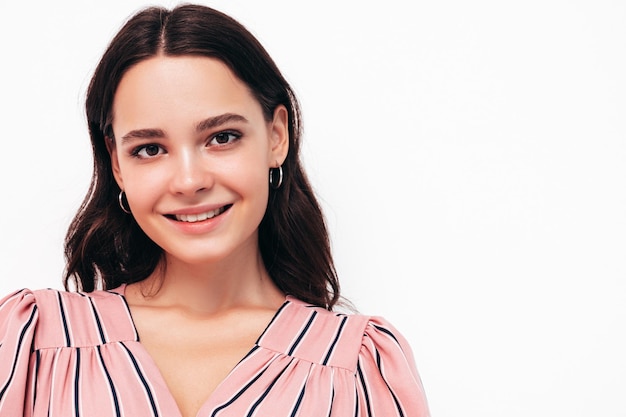 Portrait de beauté de mode de jeune femme brune avec un maquillage élégant naturel et une peau propre parfaite Modèle sexy avec de longs cheveux bouclés qui pose en studio sur fond rose Toucher ses cheveux