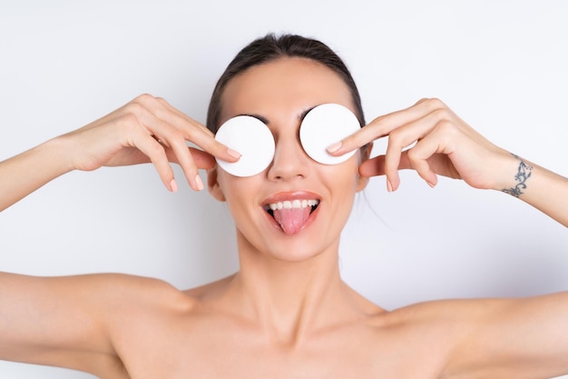 Portrait de beauté proche d'une femme aux seins nus avec une peau parfaite et un maquillage naturel enlevant des tampons de coton sur un fond blancx9