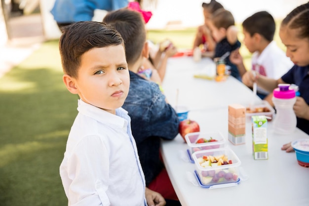 Portrait d'un bel élève d'âge préscolaire hispanique mangeant des aliments sains pendant sa pause déjeuner