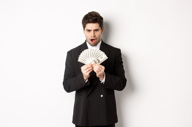 Portrait d'un bel homme d'affaires en costume tendance, l'air surpris par l'argent, a remporté un prix, debout sur fond blanc.