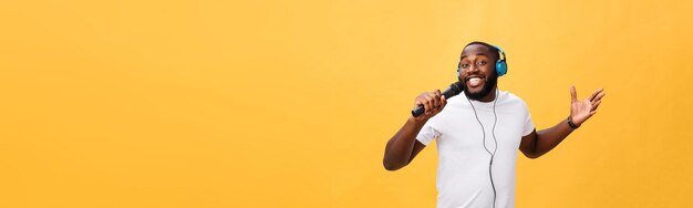 Portrait d'un bel homme africain chic positif joyeux tenant un microphone et ayant des écouteurs sur