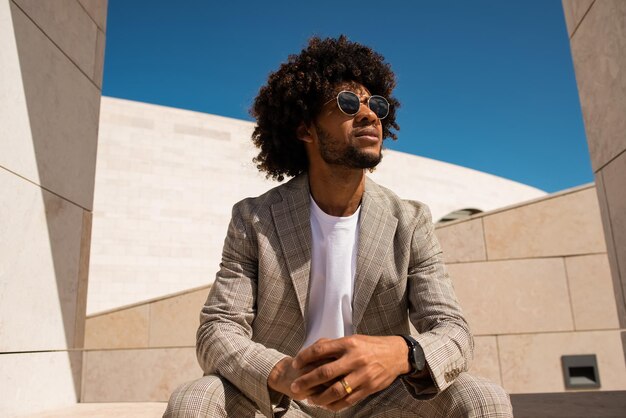 Portrait d'un bel homme afro-américain à l'extérieur. Homme en costume avec barbe assis en terrasse ou sur les toits. Portrait, concept de vie urbaine