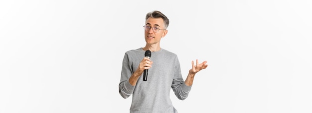 Portrait d'un bel homme d'âge moyen dans des verres et un pull gris faisant un discours parlant avec un microphon