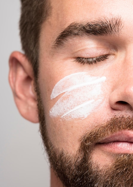 Portrait de bel homme à l'aide de gros plan de crème pour le visage