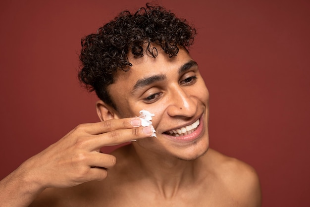 Portrait d'un bel homme appliquant une crème hydratante sur son visage et souriant