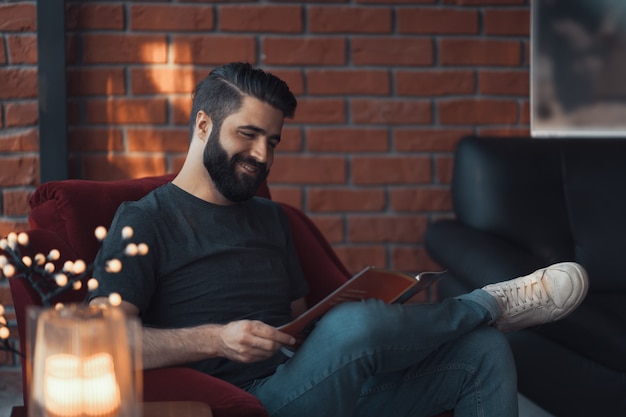 Portrait bel homme barbu portant des vêtements décontractés, assis dans une chaise rouge loft moderne