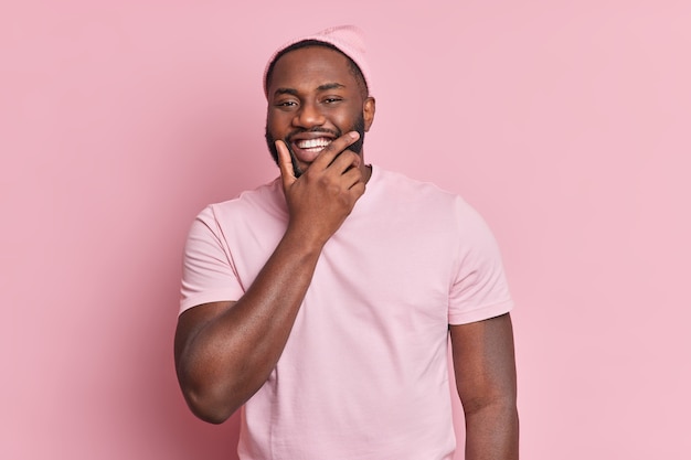 Portrait de bel homme barbu tient le menton sourit largement d'être de bonne humeur