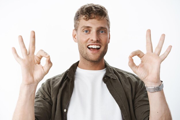 Portrait d'un bel homme blond insouciant avec des poils et des yeux bleus montrant des gestes corrects et souriant satisfait