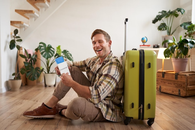 Photo gratuite portrait d'un bel homme charismatique touriste avec une valise assis sur le sol tient le passeport et le vol