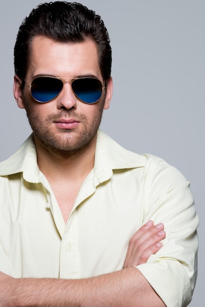 Portrait de bel homme en chemise jaune portant des lunettes de soleil avec des poses de bras croisés