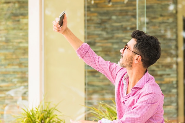 Portrait de bel homme en chemise rose prenant selfie sur téléphone mobile