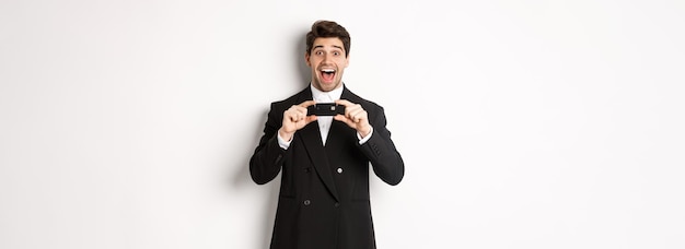 Photo gratuite portrait d'un bel homme étonné en costume noir montrant une carte de crédit et recommandant une banque debout au-dessus
