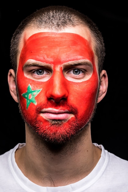 Portrait de bel homme face supporter fan de l'équipe nationale du Maroc avec le visage du drapeau peint isolé sur fond noir. Émotions des fans.