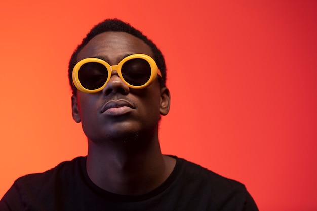 Photo gratuite portrait de bel homme avec des lunettes de soleil sur fond orange