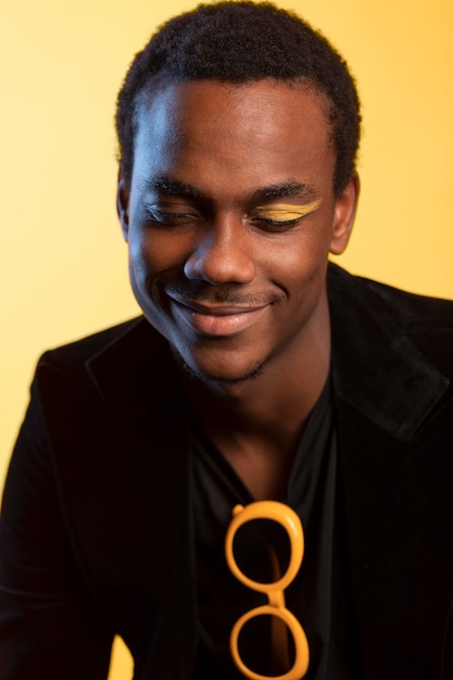 Photo gratuite portrait d'un bel homme avec des lunettes de soleil et maquillage des yeux sur fond jaune