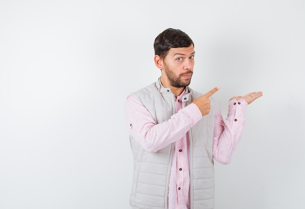 Portrait d'un bel homme montrant un geste de bienvenue, pointant vers le côté droit en gilet, chemise et semblant confiant